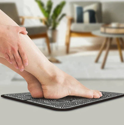 Person using EMS foot stimulation pad with black patterned surface for pain relief and muscle therapy