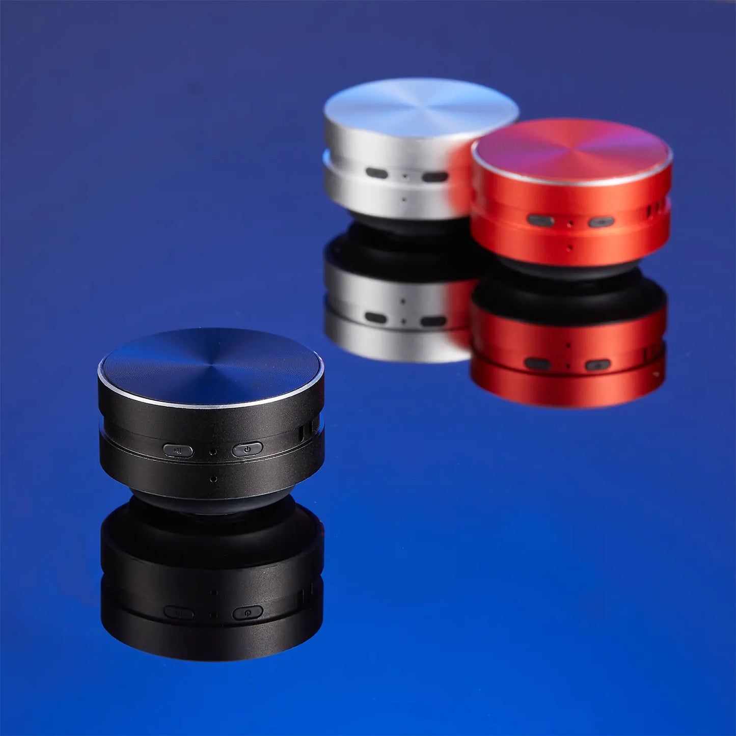 Three portable conduction speaker devices in black red and silver colors placed on reflective surface