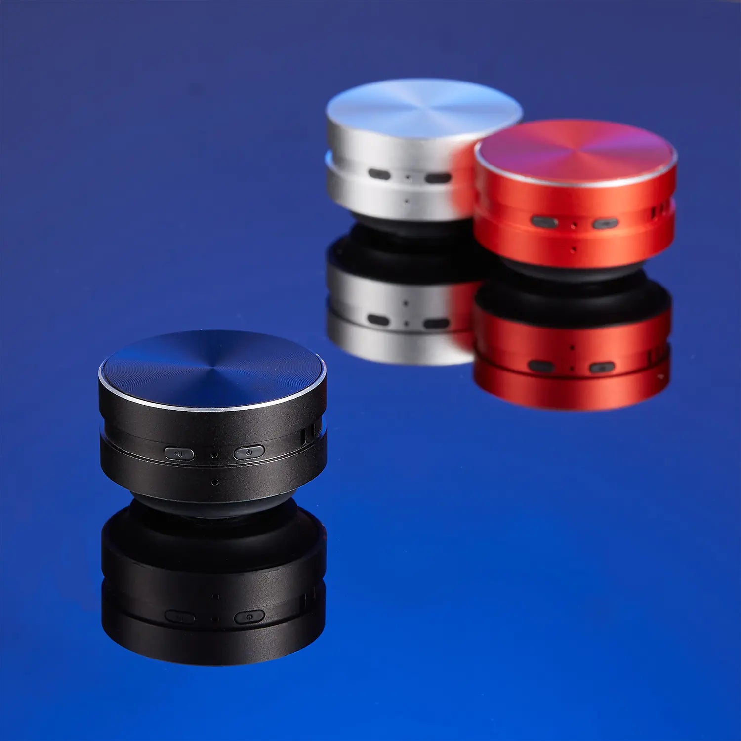 Three portable conduction speaker devices in black red and silver colors placed on reflective surface